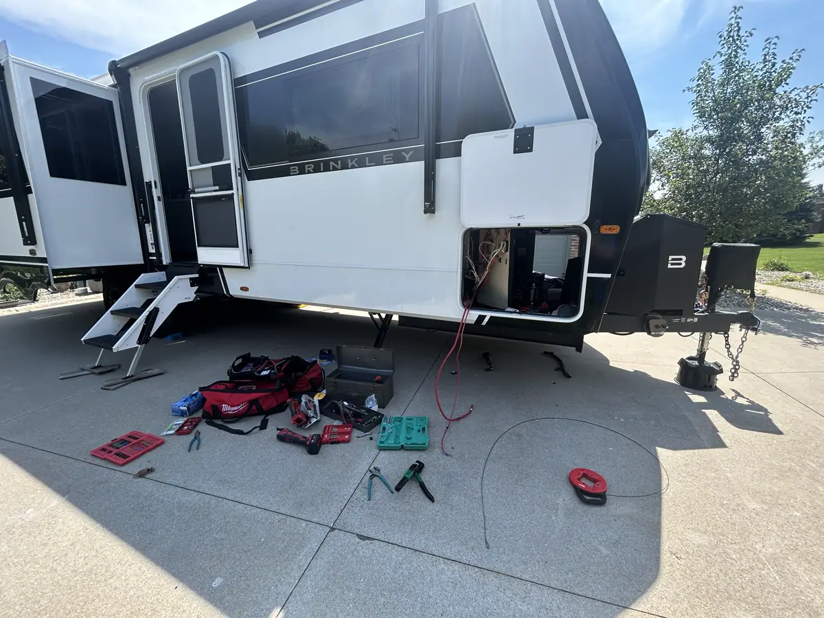 Brinkley fifth-wheel on a driveway with an open electrical bay and technician tools laid out for mobile service.
